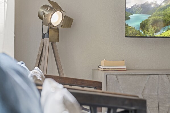 A room with a wooden desk, a lamp, a framed picture of a landscape, and a stack of books.