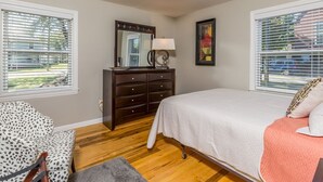 Un dormitorio con cama, cómoda, silla y ventana con persianas.