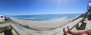 A beach view from a wooden deck with a railing, overlooking the ocean. - Beachfront Bach with Amazing Views (Pukehina)