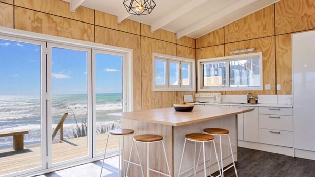 Una cocina moderna con una isla grande, taburetes de bar y vista al océano.