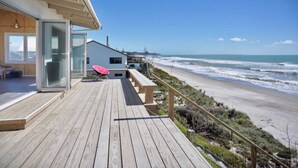 Una terraza de madera con un ventanal de vidrio que da a una playa y olas.