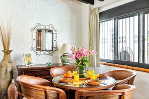 Un coin repas avec des chaises en osier, une table ronde, un vase de fleurs et un miroir au mur.