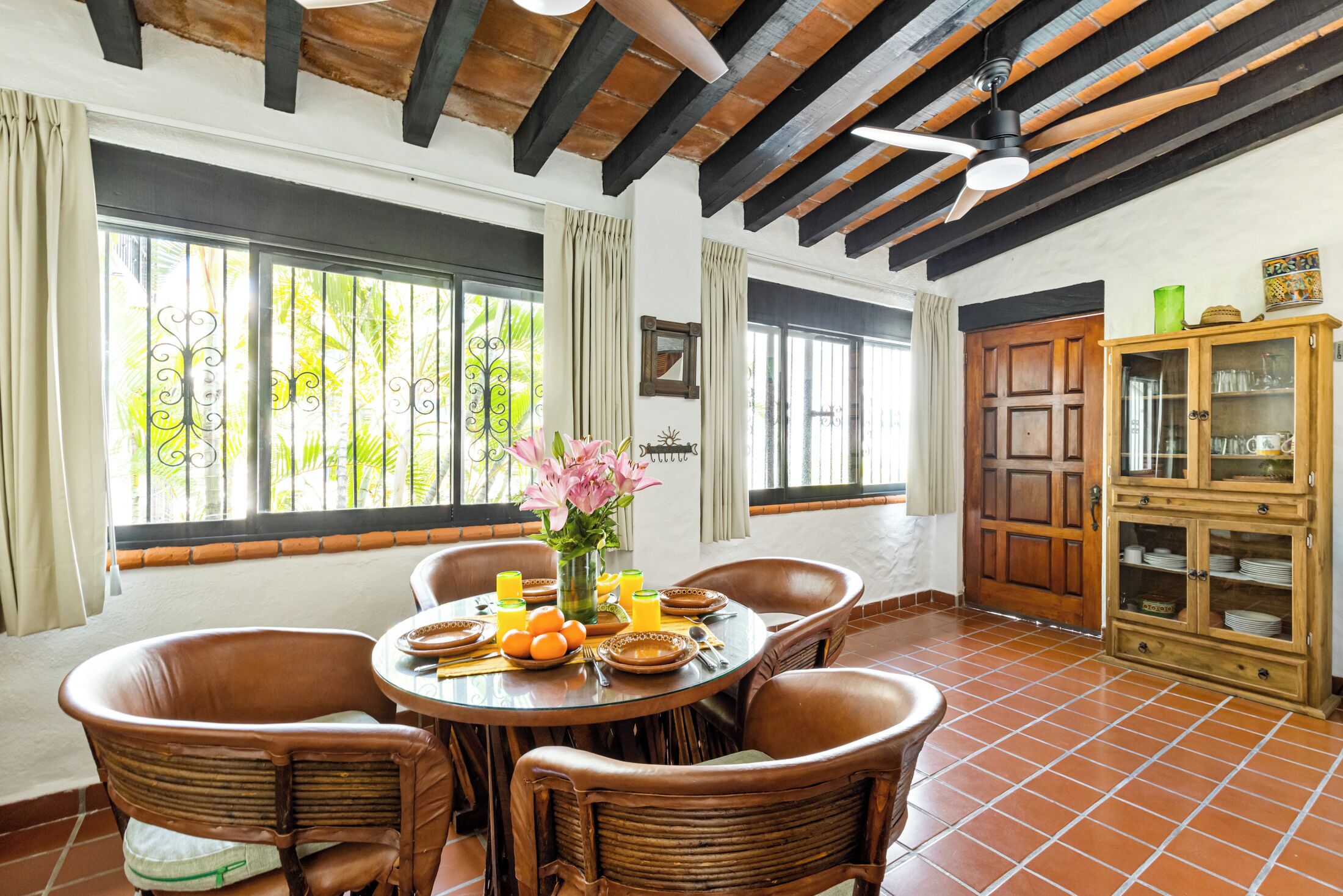A dining area with a round table, wicker chairs, and a ceiling fan.