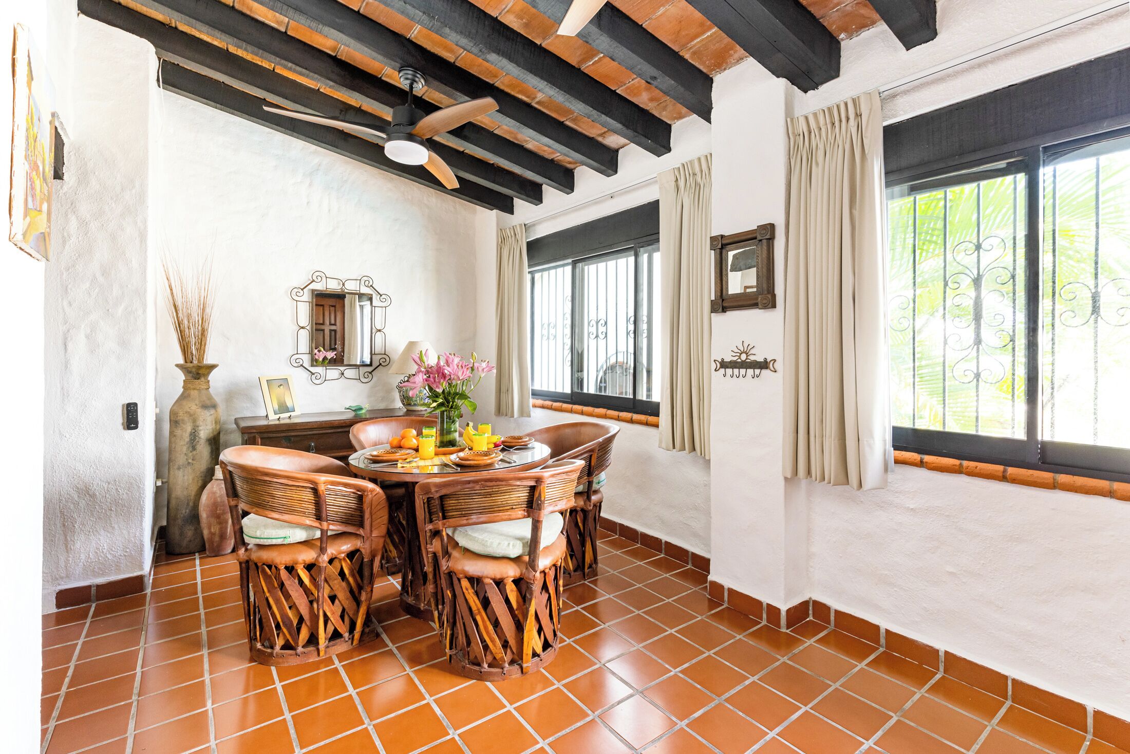 A dining area with a round table, wicker chairs, and a vase with flowers.