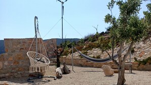 Un espacio al aire libre rústico con una hamaca, paredes de piedra y un paisaje rocoso.