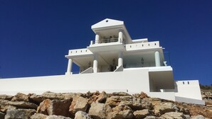 Un edificio moderno de color blanco con techo plano y varios niveles, que destaca por una columna central prominente y un balcón en el nivel superior.