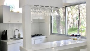 Eine moderne Küche mit weißen Schränken, einem eingebauten Gasherd, einem Fenster mit Blick auf Bäume und einer Bar mit Hockern.
