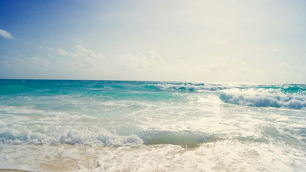 Ein Strand mit sanft brandenden Wellen unter wolkenlosem Himmel.