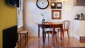 Un comedor con una mesa de madera, cuatro sillas, un reloj de pared, obras de arte enmarcadas y un jarrón con flores.
