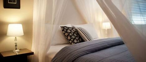 A bedroom with a canopy bed, a bedside lamp, and a framed picture on the wall.