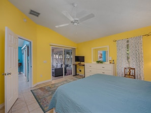 A bedroom with a bed, a ceiling fan, a dresser, a television, and a sliding glass door leading to a balcony.