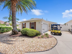 A single-story house with a garage, a palm tree, and a golf cart parked in front.
