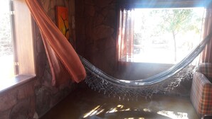 A hammock in a room with stone walls, a window with curtains, and a plaid sofa.