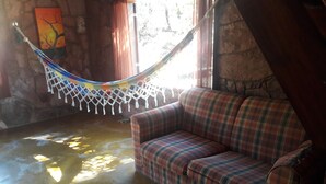 A hammock, a plaid sofa, and a stone wall with a painting.