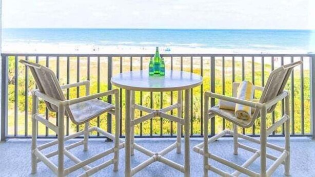 Een balkon met twee stoelen en een tafel, met uitzicht op een strand.
