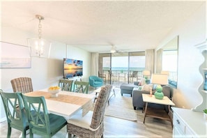 Relax in this spacious living area with a dining table for four, a large flat-screen TV, and a balcony offering ocean views.