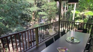 Ein überdachter Außenbereich mit Tisch und Stühlen, umgeben von einer Holzterrasse und einem Geländer.