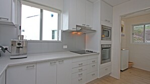 Une cuisine moderne avec des meubles blancs, un four encastré, un micro-ondes et une machine à café.