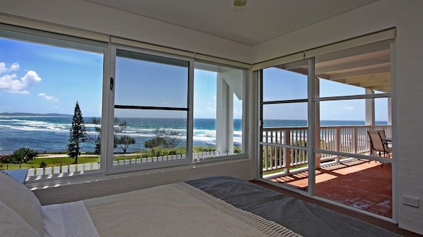 A bedroom with a large window overlooking the ocean, a balcony with a view of the sea, and a bed with a view.