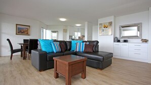 Un salon moderne avec un canapé d’angle, une table basse en bois et un coin repas comprenant des chaises et une table.