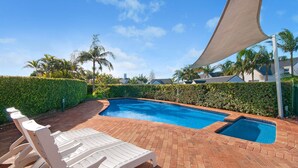 Une piscine avec une terrasse en briques et des chaises longues.