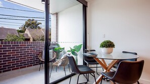 A modern balcony with a glass table, chairs, and potted plants.