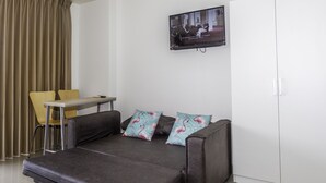 Un espacio habitable compacto con un sofá, una mesita y un televisor montado en la pared.