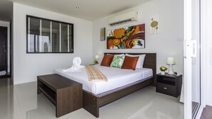 Un dormitorio de hotel moderno con una cama grande, una mesita de noche, una mesita auxiliar pequeña con una lámpara y un equipo de aire acondicionado en la pared.