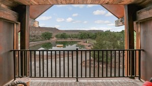 A wooden balcony with a metal railing overlooking a calm river and a mountainous landscape. - Zion Red Rock Oasis. (Rockville)