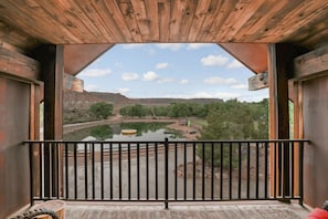A wooden balcony with a metal railing overlooking a calm river and a mountainous landscape. - Zion Red Rock Oasis. (Rockville)