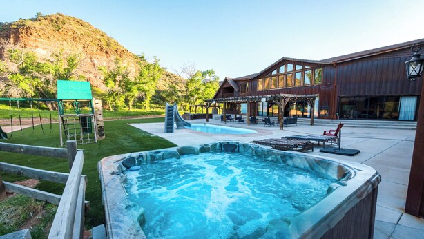 A hot tub, outdoor seating, and a building with large windows. - Zion Red Rock Oasis. (Rockville)