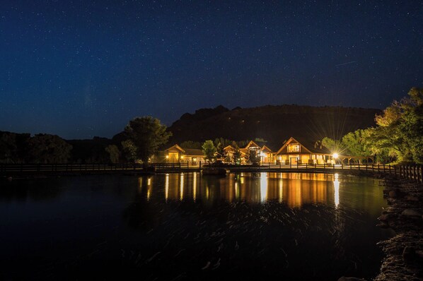 A lakeside lodge with multiple wooden cabins, a wooden dock, and a clear night sky.