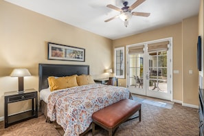 A bedroom with a bed, bedside tables, a ceiling fan, a window with a view, and a door leading outside.