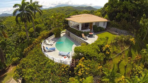 A house with a swimming pool surrounded by lush greenery and a view of distant mountains.