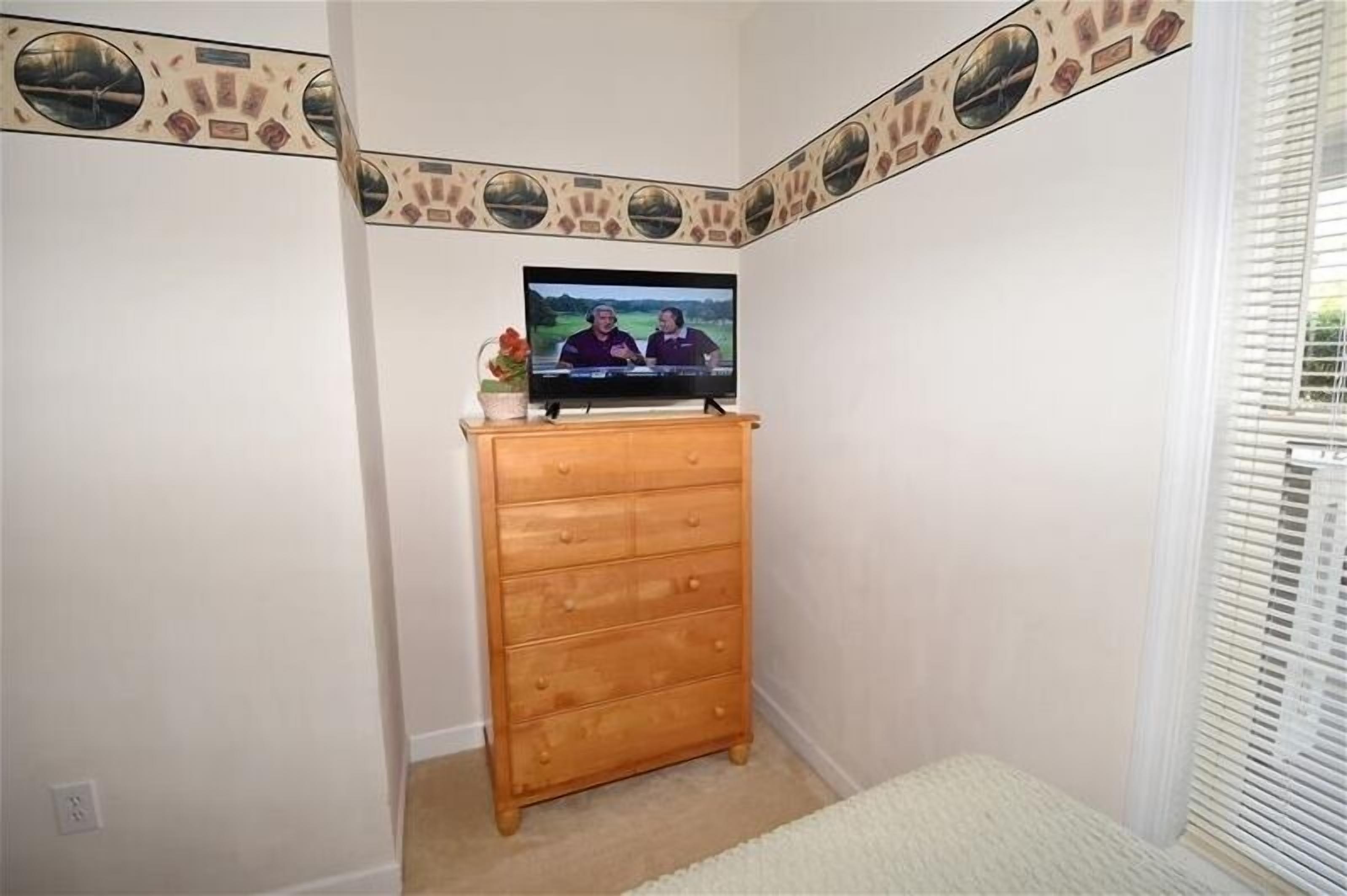 A corner room with a wooden dresser, a television on top, and a patterned ceiling.