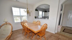 Uma sala de jantar com uma mesa retangular rodeada por seis cadeiras de madeira, um lustre e uma janela com persianas.