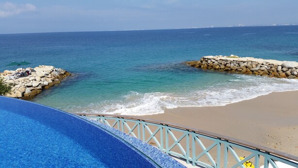 A beach with clear blue water, a sandy shore, and a stone wall.