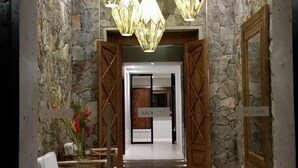 A reception area with stone walls, wooden doors, and a chandelier. There are two large vases and a reception desk with chairs.