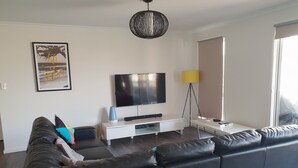 Een moderne woonkamer met een zwarte leren bank, een flatscreen-tv, een witte tv-meubel en een vloerlamp.