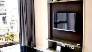 Ein modernes Wohnzimmer mit einem an der Wand befestigten Flachbildfernseher, einem eleganten schwarzen Couchtisch und einem großen Fenster mit Blick auf eine Skyline.