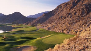 A golf course with a water hazard, surrounded by rocky terrain and mountains.