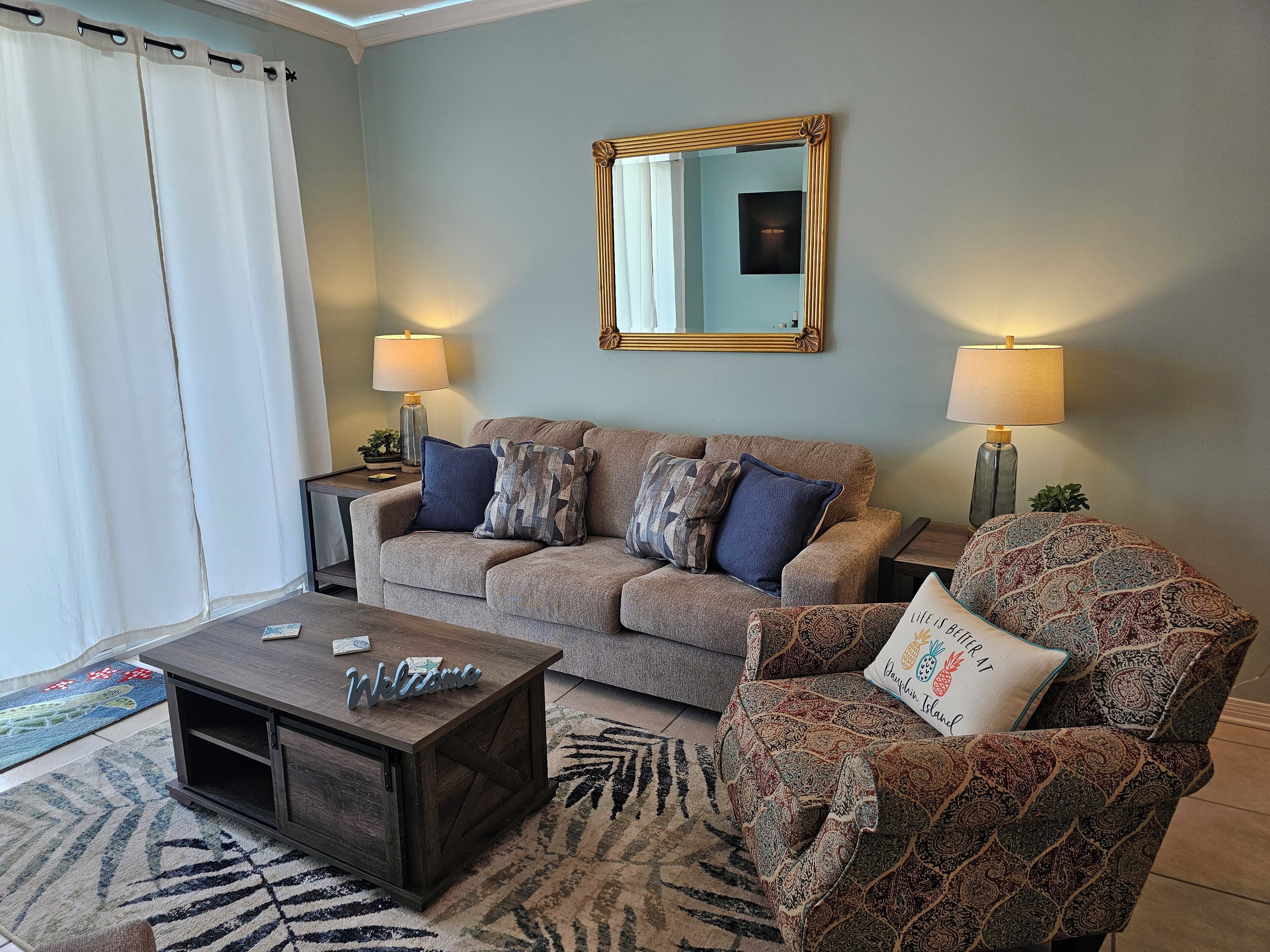 A living room with a sofa, armchair, coffee table, lamps, and a mirror on the wall.