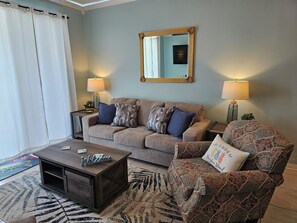 A living room with a sofa, armchair, coffee table, lamps, and a mirror on the wall. - Inn at Dauphin Island 309 Wonderful Unit with Expansive Views!! (Dauphin Island)