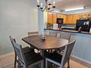 A dining area with a round wooden table, six chairs, a chandelier, and wooden cabinets in the background.