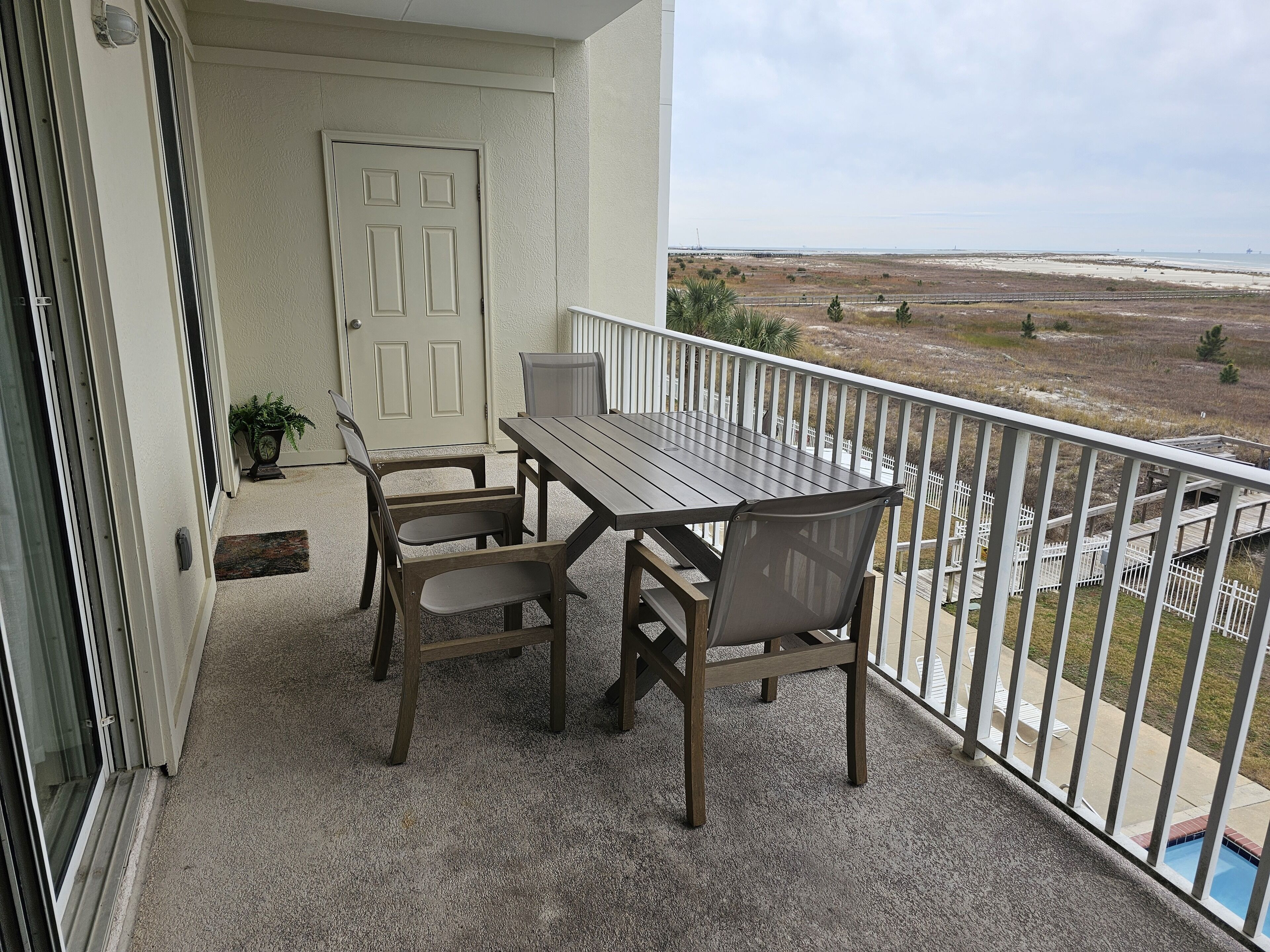 Varanda com mesa e cadeiras, uma porta e vista para a praia e oceano.