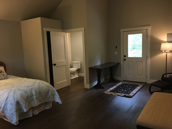 A bedroom with a bed, a door leading to a bathroom, a bench, and a lamp.