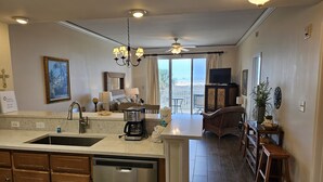 A kitchen with a dishwasher, a coffee maker, and a dining area with a table and chairs. - Inn at Dauphin Island 203 Beautifully Furnished with Great Views!! (Dauphin Island)