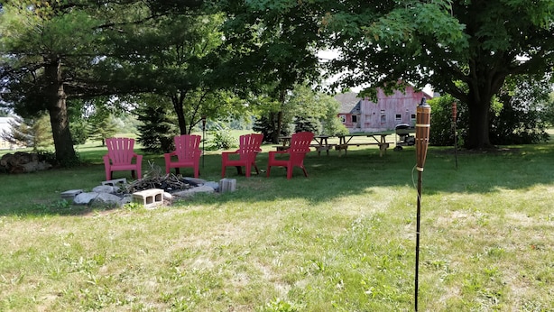 Un espacio al aire libre con césped, mesas de picnic y sillas rojas, y un banco de madera, además de un poste alto.