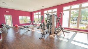 Uma academia com equipamentos de exercício, janelas amplas e uma parede vermelha.