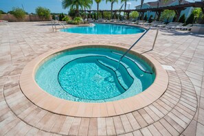 Relax by the pool with a hot tub and a larger pool surrounded by lounge chairs and umbrellas.